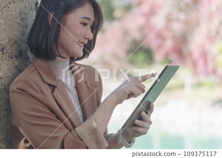 Asian woman hands using digital tablet shopping online outdoors in autumn green park. Female hand touching pointing smart tablet using mobile app work travel. Beautiful Asian woman Smart technology Asian woman hands using digital tablet shopping online outdoors in autumn green park. Female hand touching pointing smart tablet using mobile app work travel. Beautiful Asian woman Smart technology 109375117
