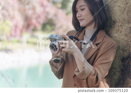 Asian Women with vintage film camera take a photo. Smiling female photographer look at photo from professional camera outdoor. Young woman shooting photo in green nature park. Beautiful woman hobby Asian Women with vintage film camera take a photo. Smiling female photographer look at photo from professional camera outdoor. Young woman shooting photo in green nature park. Beautiful woman hobby 109375120