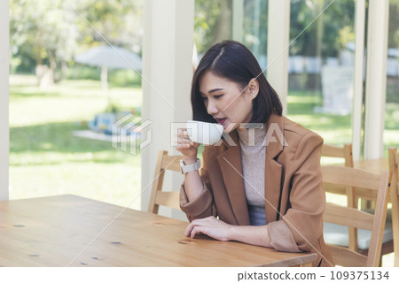 Asian Woman drink black coffee hand holding cup at green garden cafe. Young woman smile face love drink coffee. Beauty woman drinking black coffee in coffee shop holding freshness cup. Coffee lover 109375134