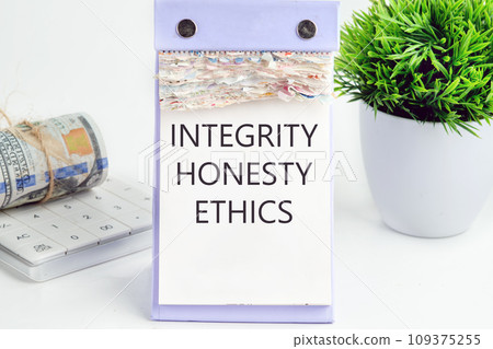 INTEGRITY HONESTY ETHICS text, word, inscription on a desktop calendar on a white background next to money and a green flower 109375255