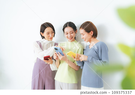 A group of middle-aged women talking while looking at their smartphones 109375337