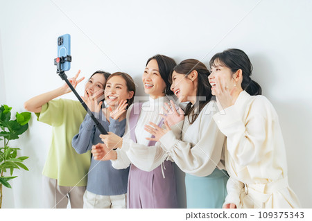 Casual group of women taking selfies with selfie sticks 109375343