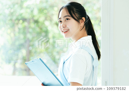 Young female caregiver standing by the window Young female caregiver standing by the window 109379182