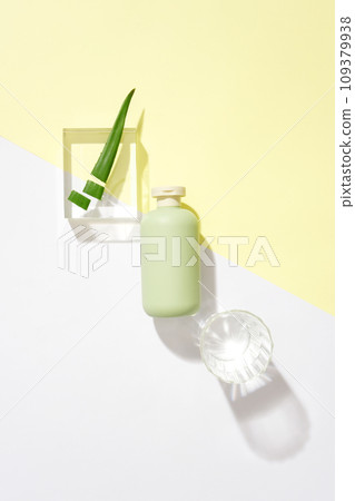 An unlabeled cosmetic bottle, a glass of water and fresh aloe vera is displayed on a glass podium on a pastel background. Creative space for advertising. An unlabeled cosmetic bottle, a glass of water and fresh aloe vera is displayed on a glass podium on a pastel background. Creative space for advertising. 109379938