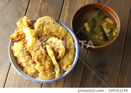 A tempura bowl with lots of ingredients such as shrimp, chikuwa, green beans, pumpkin, sweet potato, and lotus root, and miso soup. 109381246