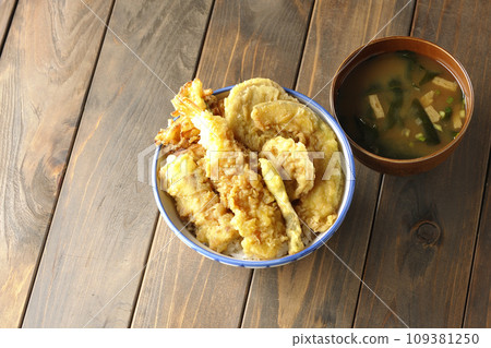A tempura bowl with lots of ingredients such as shrimp, chikuwa, green beans, pumpkin, sweet potato, and lotus root, and miso soup. 109381250