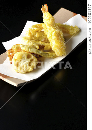 Assorted tempura of shrimp, chikuwa, green beans, pumpkin, sweet potato, and lotus root photographed against a black background 109381567