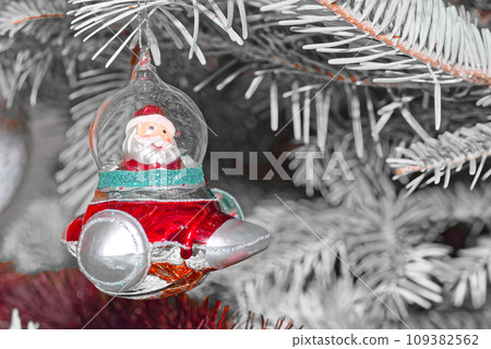 Santa Claus in a spaceship as Christmas tree decoration against white branches Santa Claus in a spaceship as Christmas tree decoration against white branches 109382562