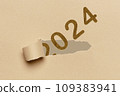 2024, Number 2024 appearing through the tear in a brown cardboard. Happy New Year 109383941