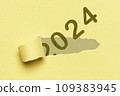 2024, Number 2024 appearing through the tear in a yellow cardboard. Happy New Year 109383945