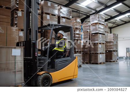 Multiracial warehouse worker driving forklift. Warehouse worker preparing products for shipmennt, delivery, checking stock in warehouse. 109384827
