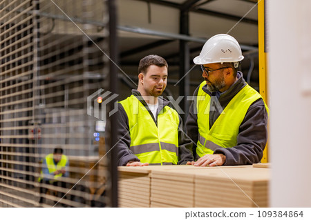 Young man with Down syndrome working in modern factory, colleague teaching him about his job, showing process. Concept of workers with disabilities, support in workplace. 109384864