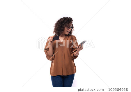 young smart pretty brunette woman dressed in a brown shirt uses a mobile phone and holds a plastic young smart pretty brunette woman dressed in a brown shirt uses a mobile phone and holds a plastic 109384938