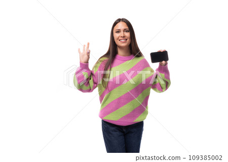 young pretty caucasian woman with black hair dressed in a pink sweater shows the screen of a 109385002