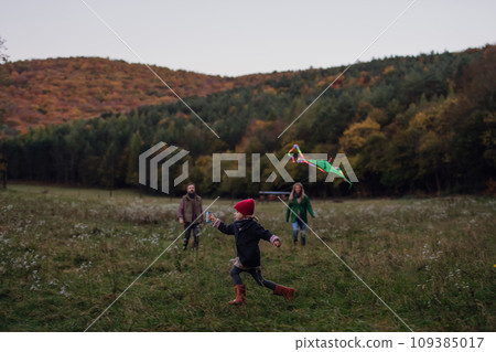 Girl flying kite on meadow, running, having fun with parents. Autumn windy weather for kite flying. 109385017