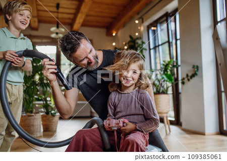 Father and son vacuuming girl's hair with vacuum cleaner. Father with kids cleaning house, helping with house chores. Father and son vacuuming girl's hair with vacuum cleaner. Father with kids cleaning house, helping with house chores. 109385061