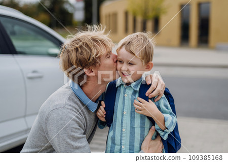 Father saying goodbyeto to son in front of school building, hugging him and kissing him on the cheek. Dad heading to work. Concept of work-life balance for parents. 109385168