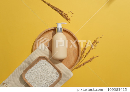 Square dish of rice placed on a scarf. Blank label pump bottle displayed on a wooden tray on yellow background. Container packaging of skin care branding 109385415