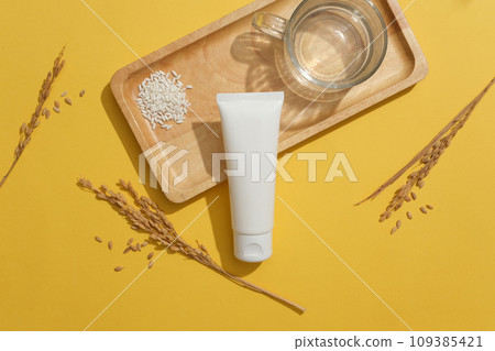 Wooden tray featured a handful of white rice, glass of water and a cosmetic tube. Few wheat ears displayed. Natural beauty blank label for branding mock-up concept Wooden tray featured a handful of white rice, glass of water and a cosmetic tube. Few wheat ears displayed. Natural beauty blank label for branding mock-up concept 109385421