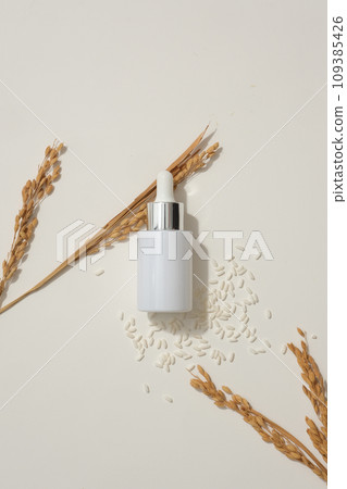 Glass bottle with dropper arranged over white background with rice and wheat ears. Mockup design. Rice water is known to help reduce skin irritation Glass bottle with dropper arranged over white background with rice and wheat ears. Mockup design. Rice water is known to help reduce skin irritation 109385426