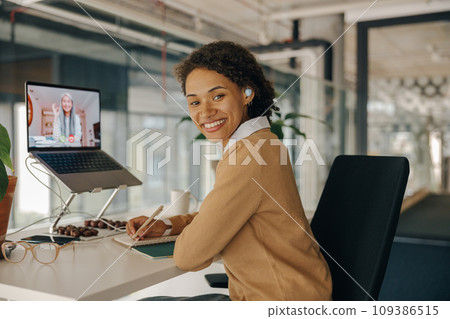 Female freelancer have video conference with client and making notes sitting in cozy coworking 109386515