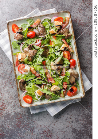 Fresh fried chicken liver salad with arugula, onions, tomatoes, croutons and bacon close-up in a plate. Vertical top view 109387556