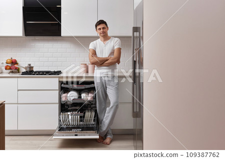 handsome positive man using dishwasher and washing dishes in white modern kitchen. copy space 109387762