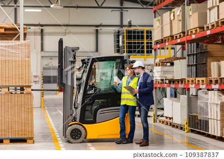 Female forklift driver, warehouse worker talking with manager, standing by forklift. Warehouse worker preparing products for shipmennt, delivery, checking stock in warehouse. 109387837