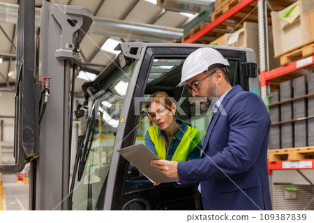 Female forklift driver talking with manager in warehouse, order picking. Warehouse worker preparing products for shipmennt, delivery, checking stock in warehouse. Female forklift driver talking with manager in warehouse, order picking. Warehouse worker preparing products for shipmennt, delivery, checking stock in warehouse. 109387839