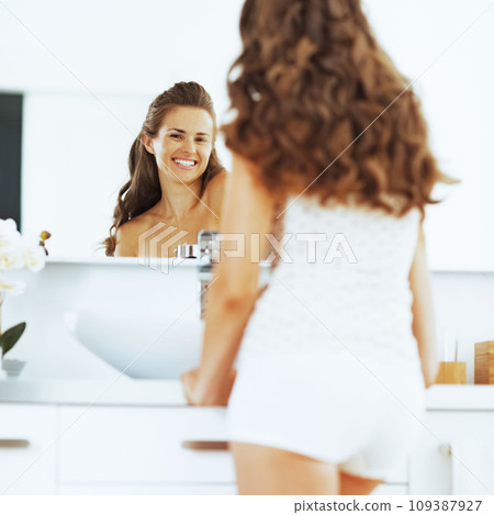 Happy young woman looking in mirror in bathroom 109387927