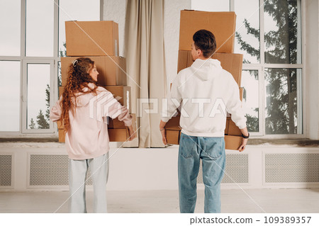 Happy young family couple man and woman moving with cardboard boxes to new estate home apartment. Rear back view. Happy young family couple man and woman moving with cardboard boxes to new estate home apartment. Rear back view. 109389357