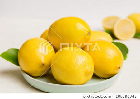Fresh cutted lemon and whole lemons over round plate on colored background. Food and drink ingredients preparing. healthy eating theme top view vith copy space 109390342