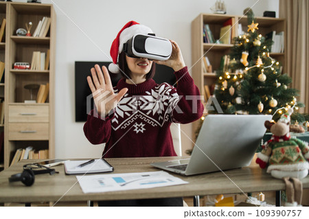 Caucasian young adult businesswoman wearing Santa hat using VR glasses Caucasian young adult businesswoman wearing Santa hat using VR glasses 109390757