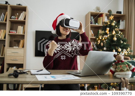 Businesswoman wearing Santa hat using VR glasses raising fist 109390770