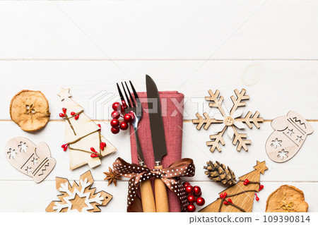 Top view of fork and knife tied up with ribbon on napkin on wooden background. Christmas decorations and New Year tree. Happy holiday concept with empty space for your design 109390814