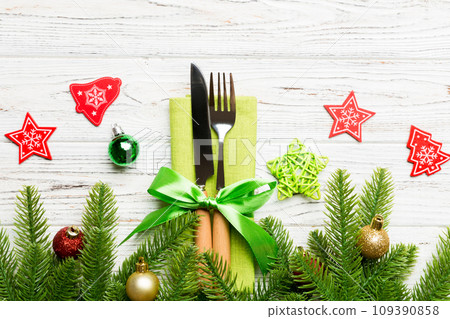 Top view of christmas decorations on wooden background. Fork and knife on napkin tied up with ribbon and empty space for your design. New year pattern concept Top view of christmas decorations on wooden background. Fork and knife on napkin tied up with ribbon and empty space for your design. New year pattern concept 109390858