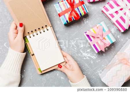 Top view of female hand opening a notebook on cement Christmas background. Wish list. New Year concept Top view of female hand opening a notebook on cement Christmas background. Wish list. New Year concept 109390880