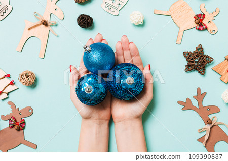 Top view of a heap of New Year balls in female hands on blue backround made of festive decorations. Christmas time concept 109390887