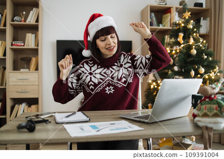 Emotional woman in Santa hat with raised hands listening to favourite songs 109391004