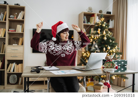 Emotional woman in Santa hat with raised hands listening to favourite songs 109391018