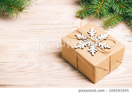 Christmas handmade gift box decorated with craft paper and white snowflake on white wooden background top view. Winter xmas holiday theme with fir branches New Year. Toned Christmas handmade gift box decorated with craft paper and white snowflake on white wooden background top view. Winter xmas holiday theme with fir branches New Year. Toned 109391045