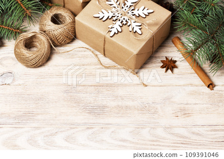 Christmas background with gift boxes wrapped in kraft paper, fir tree branches, pine cones, cinnamon and star anise on white wooden background. Flat lay, top view Christmas background with gift boxes wrapped in kraft paper, fir tree branches, pine cones, cinnamon and star anise on white wooden background. Flat lay, top view 109391046