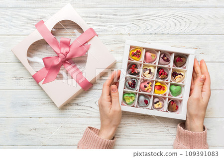Female hands with delicious candies in box on color background 109391083