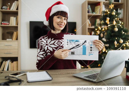Businesswoman in Santa hat looking at camera pointing at graphic materials 109391110