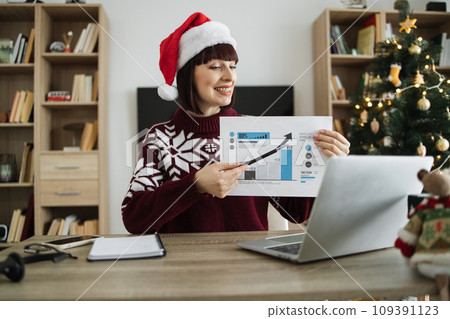 Confident mature adult businesswoman in Santa hat pointing at graphic materials 109391123