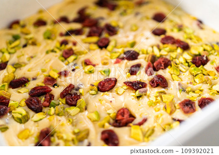 Removing cranberry pistachio fudge from a square cheesecake pan lined with parchment. 109392021