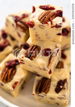 Homemade white chocolate cranberry pecan fudge pieces on a white ceramic plate. 109392056