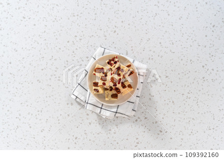 Flat lay. Homemade white chocolate cranberry pecan fudge pieces on a white ceramic plate. Flat lay. Homemade white chocolate cranberry pecan fudge pieces on a white ceramic plate. 109392160
