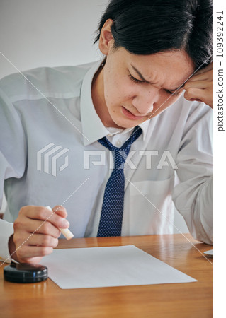 A young man stamping a document with a grimace on his face 109392241