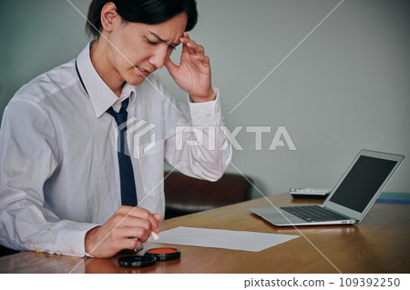 A young man stamping a document with a grimace on his face A young man stamping a document with a grimace on his face 109392250